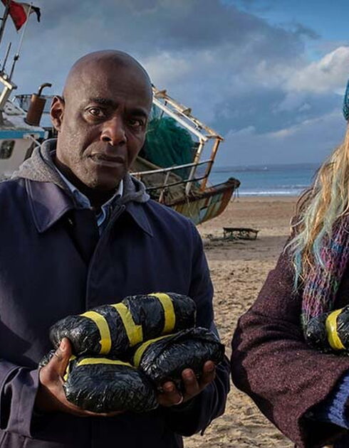 Paterson Joseph as Samuel, and Daisy Haggard as Janet, standing on beach in front of grounded boat in still from BBC’s Boat Story
